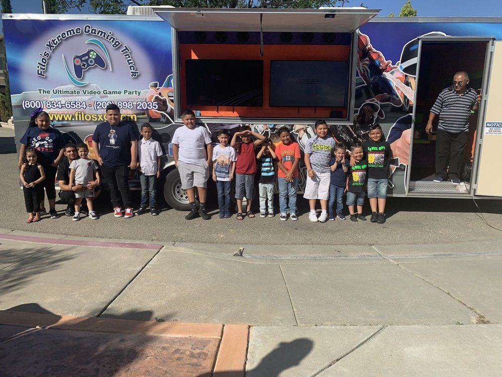Group of children and adults pose in front of a video game trailer with large screens.