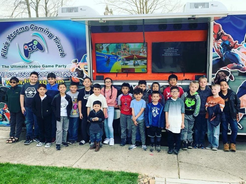Group of children standing in front of a video game party truck with screens showing gameplay.