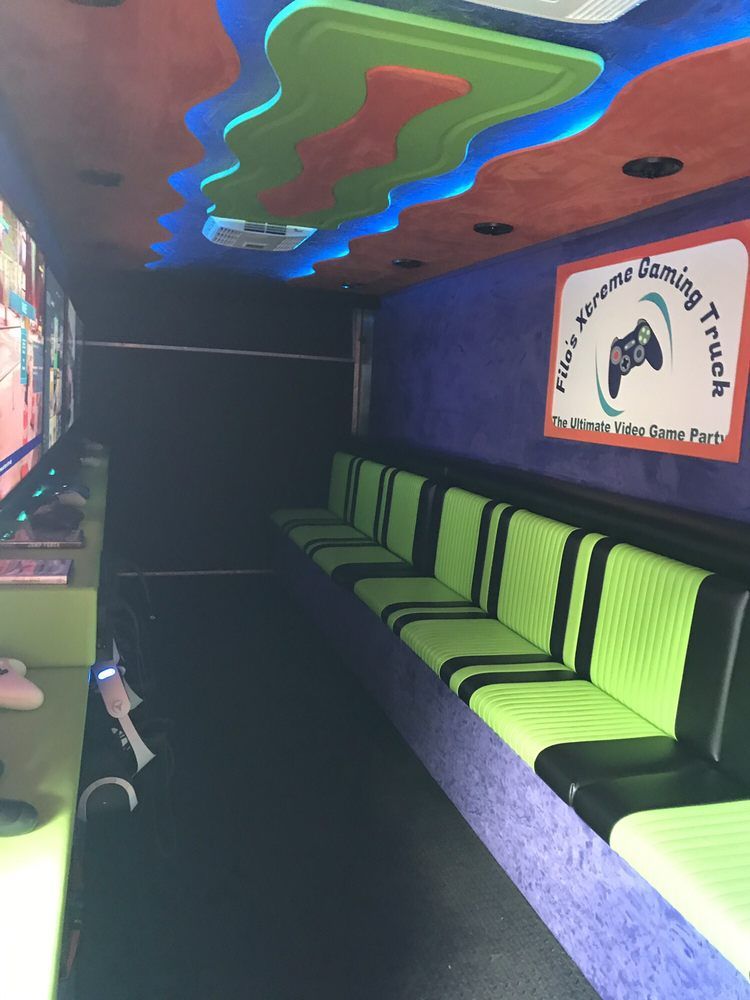 Inside of a gaming truck. Rows of green and black seating, screens, and colorful ceiling lighting.