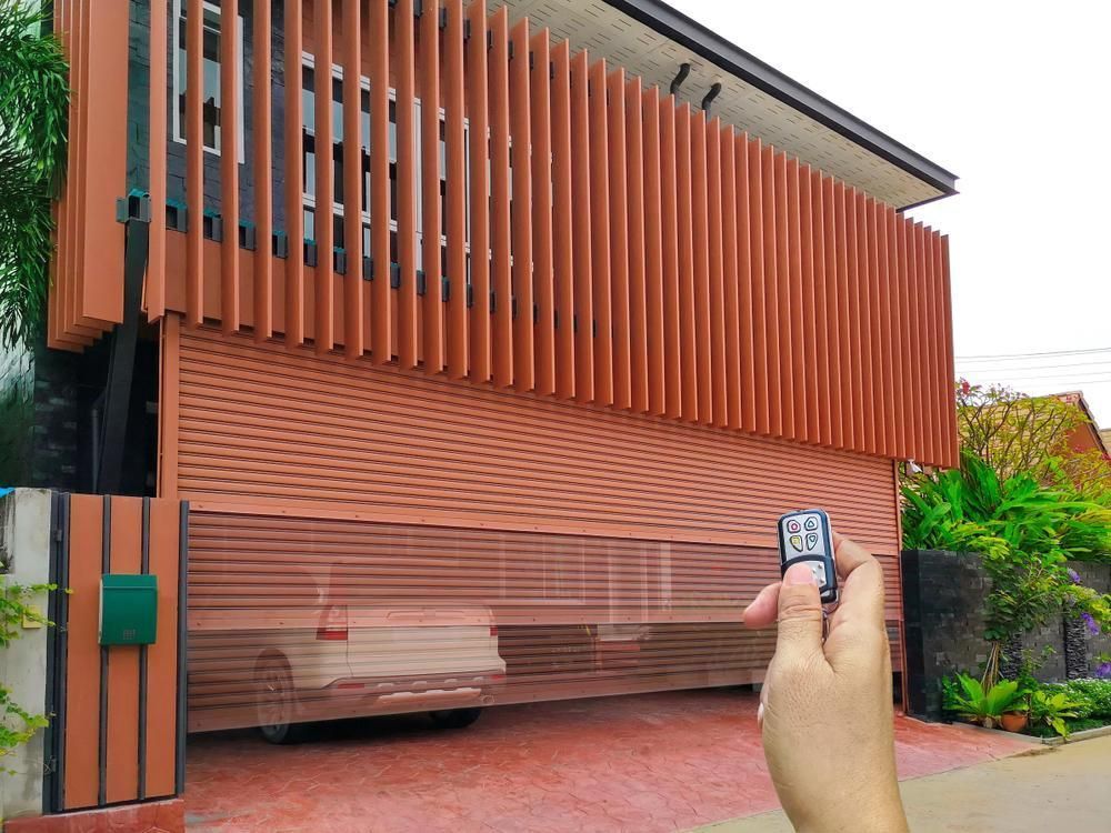 A Person Is Holding A Remote Control In Front Of A Garage Door — The Roller Door Man NQ In Portsmith, QLD