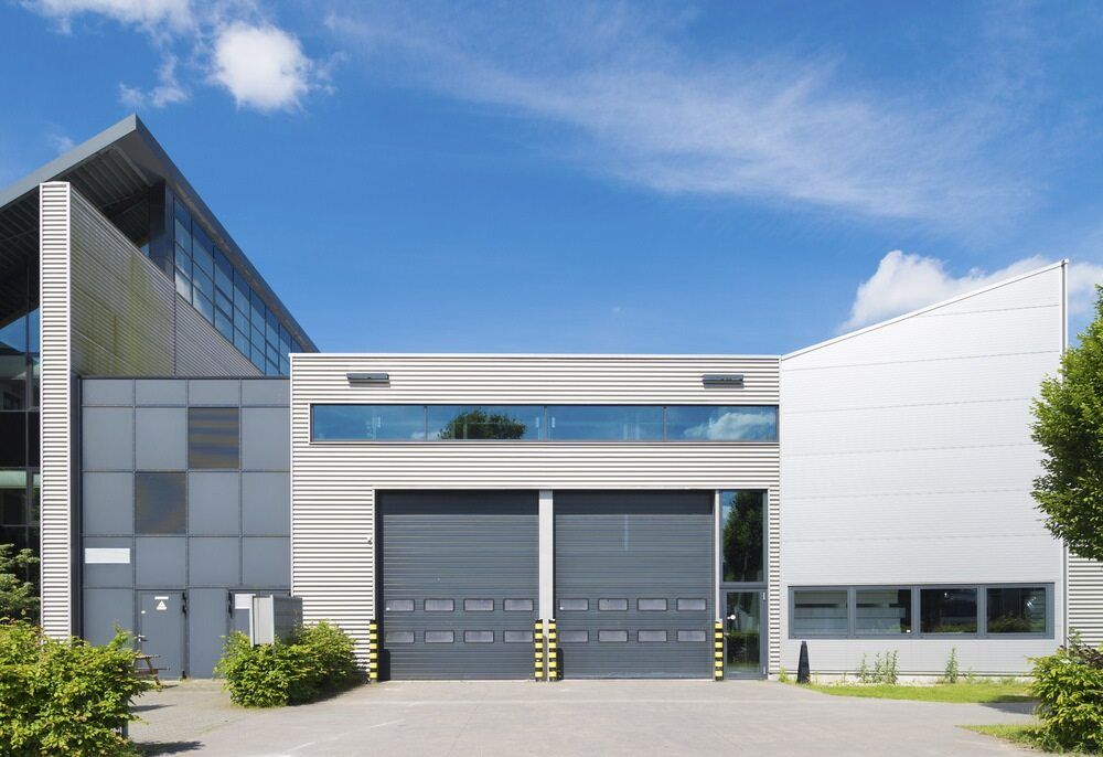A Large Industrial Building With Two Garage Doors and a Blue Sky in the Background — The Roller Door Man NQ In Atherton, QLD
