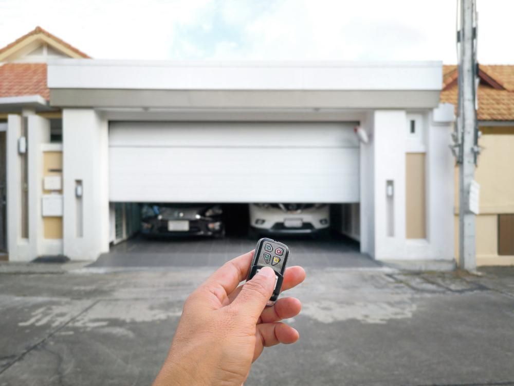A Person Is Holding A Remote Control In Front Of A Garage Door — The Roller Door Man NQ In Portsmith, QLD