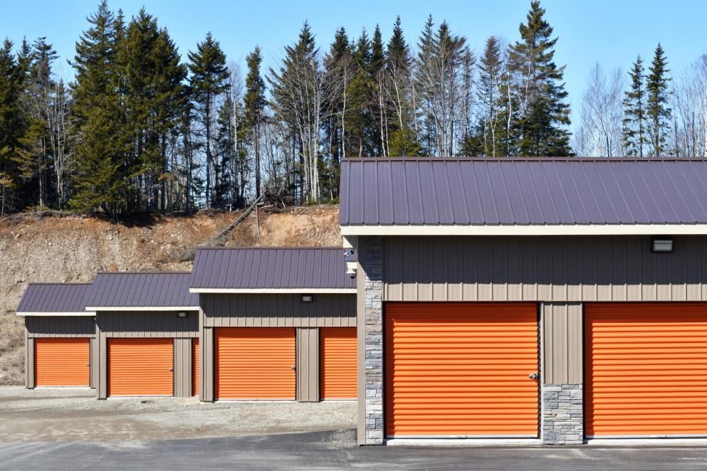 A Row Of Garages With Orange Doors And Trees In The Background — The Roller Door Man NQ In Portsmith, QLD