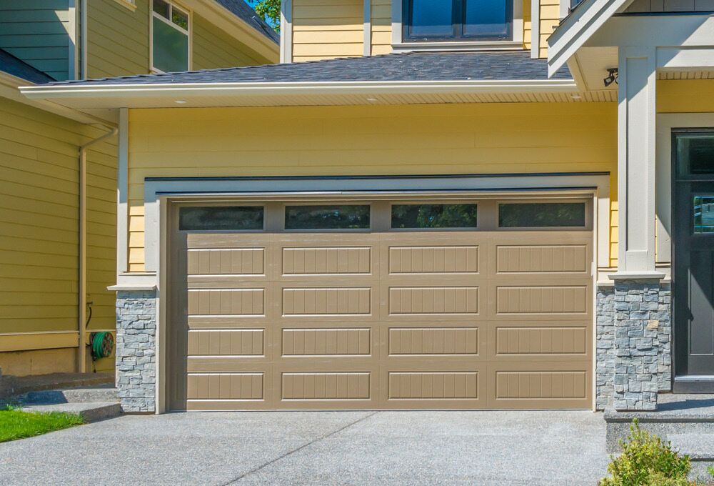 A Large Garage Door is Sitting in Front of a Yellow House — The Roller Door Man NQ In Mareeba, QLD