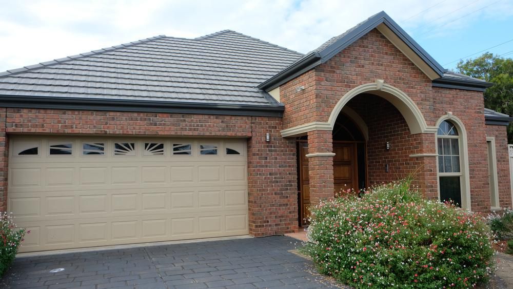 A Brick House With A Tan Garage Door And A Black Roof — The Roller Door Man NQ In Portsmith, QLD