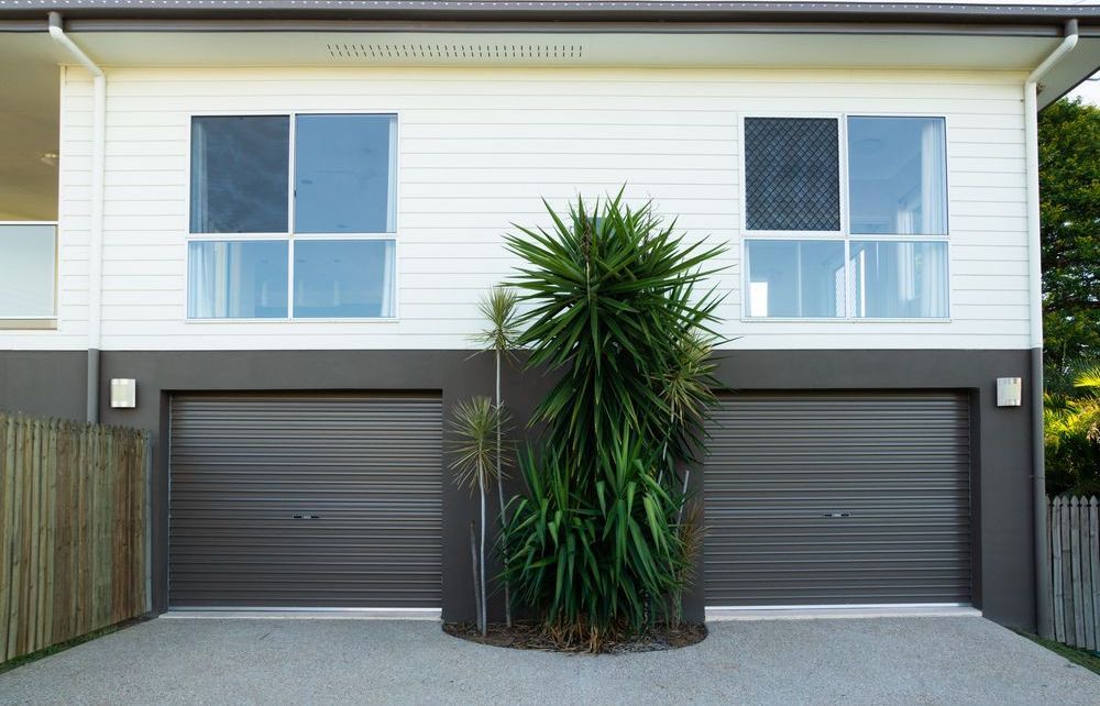 A House With Two Garages and a Palm Tree in Front of It — The Roller Door Man NQ In Palm Cove, QLD
