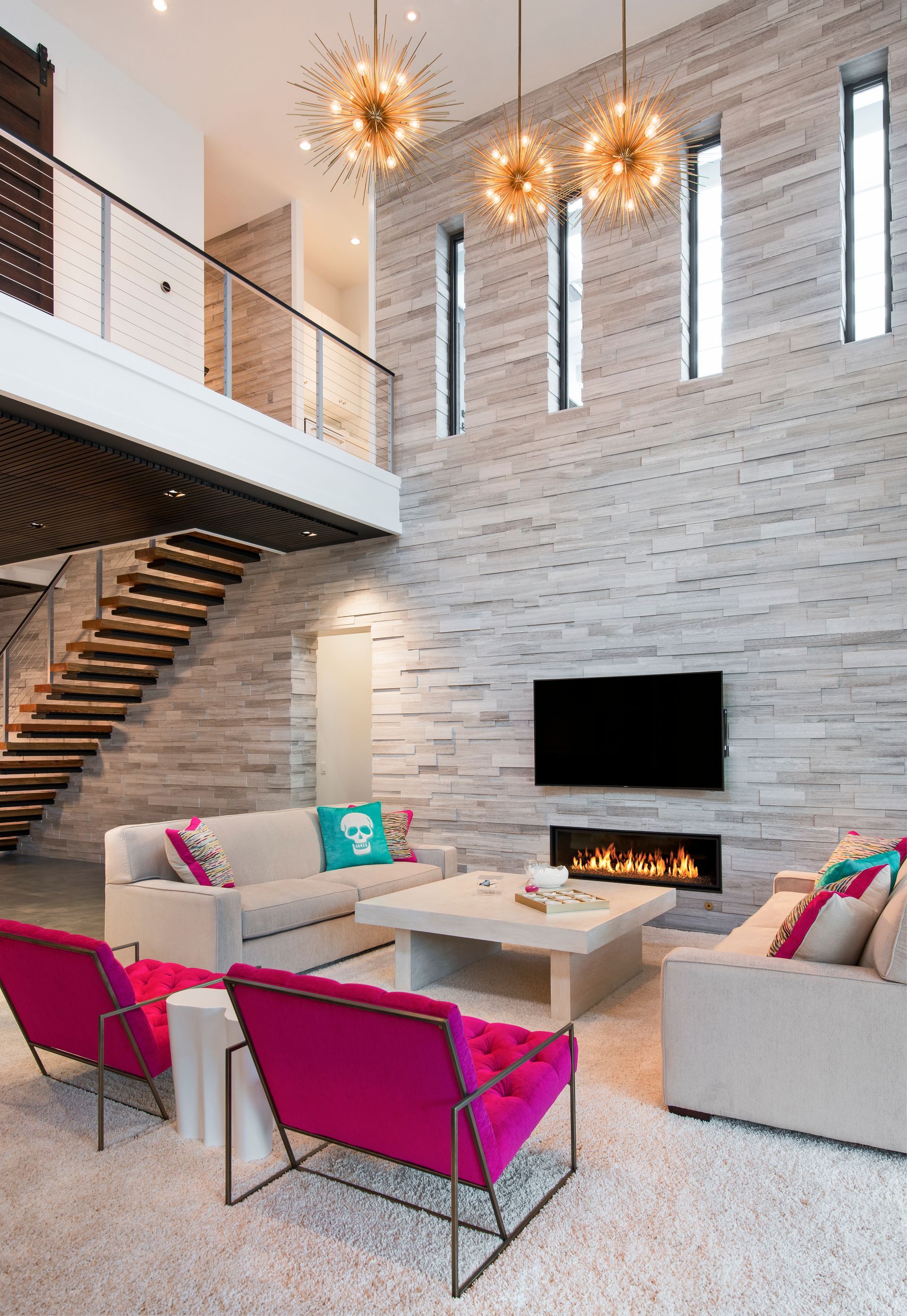 Modern living room with high ceilings, fireplace, and hot pink accent chairs.