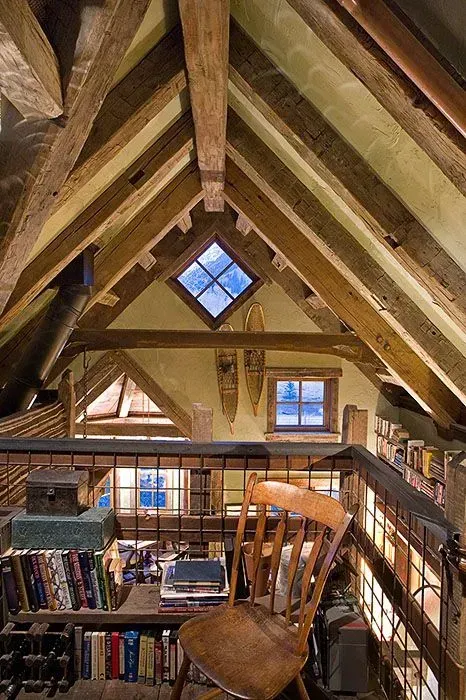 Cozy attic room with exposed wooden beams, a small window, and a wooden chair near a bookshelf.