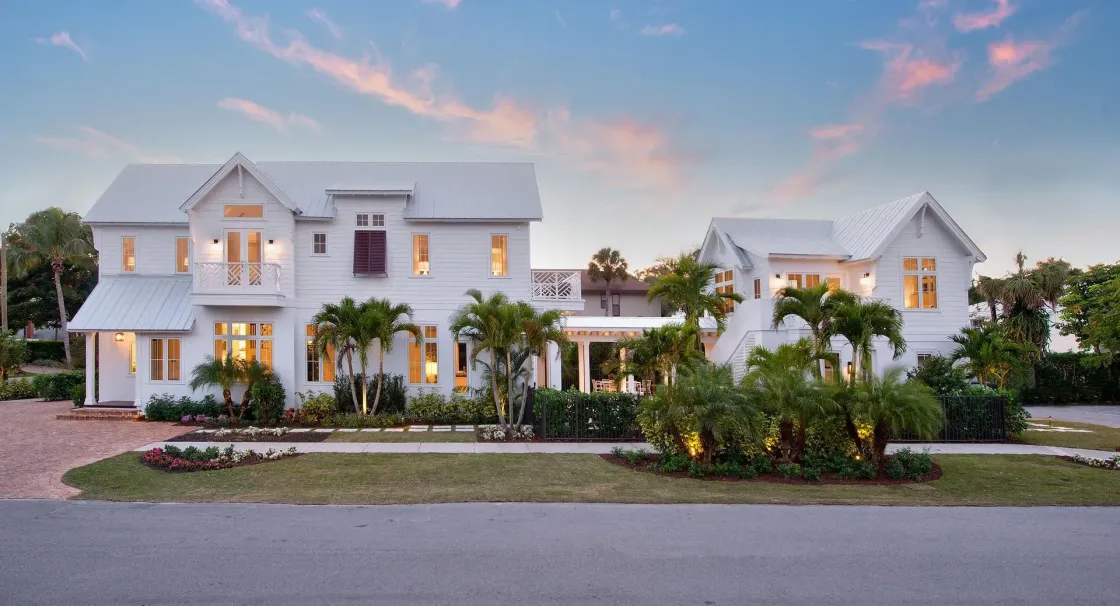 White two-story house with a matching smaller building, palm trees, and landscaped yard.