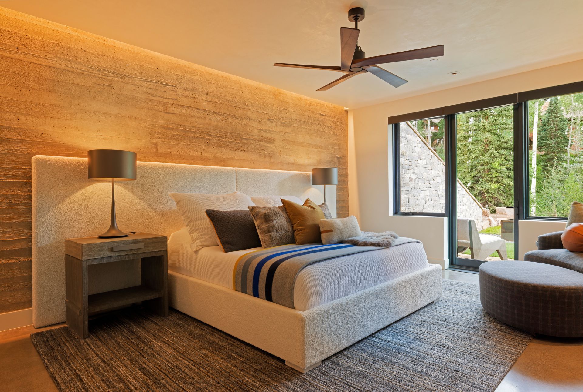 Bedroom with light wood floors, a bed, seating area, and windows with shutters.
