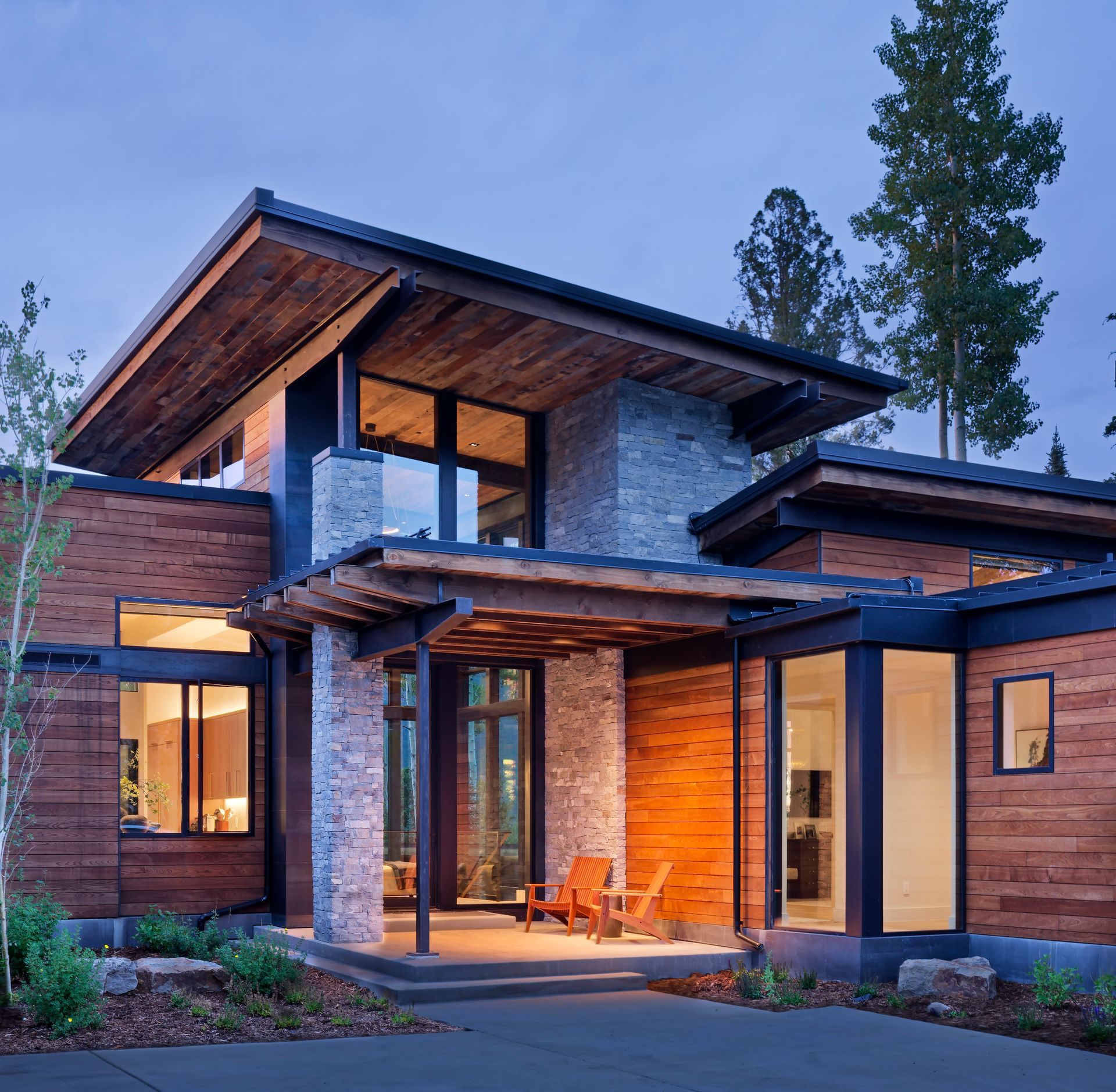 Modern stone-and-wood house with warm interior lights at dusk