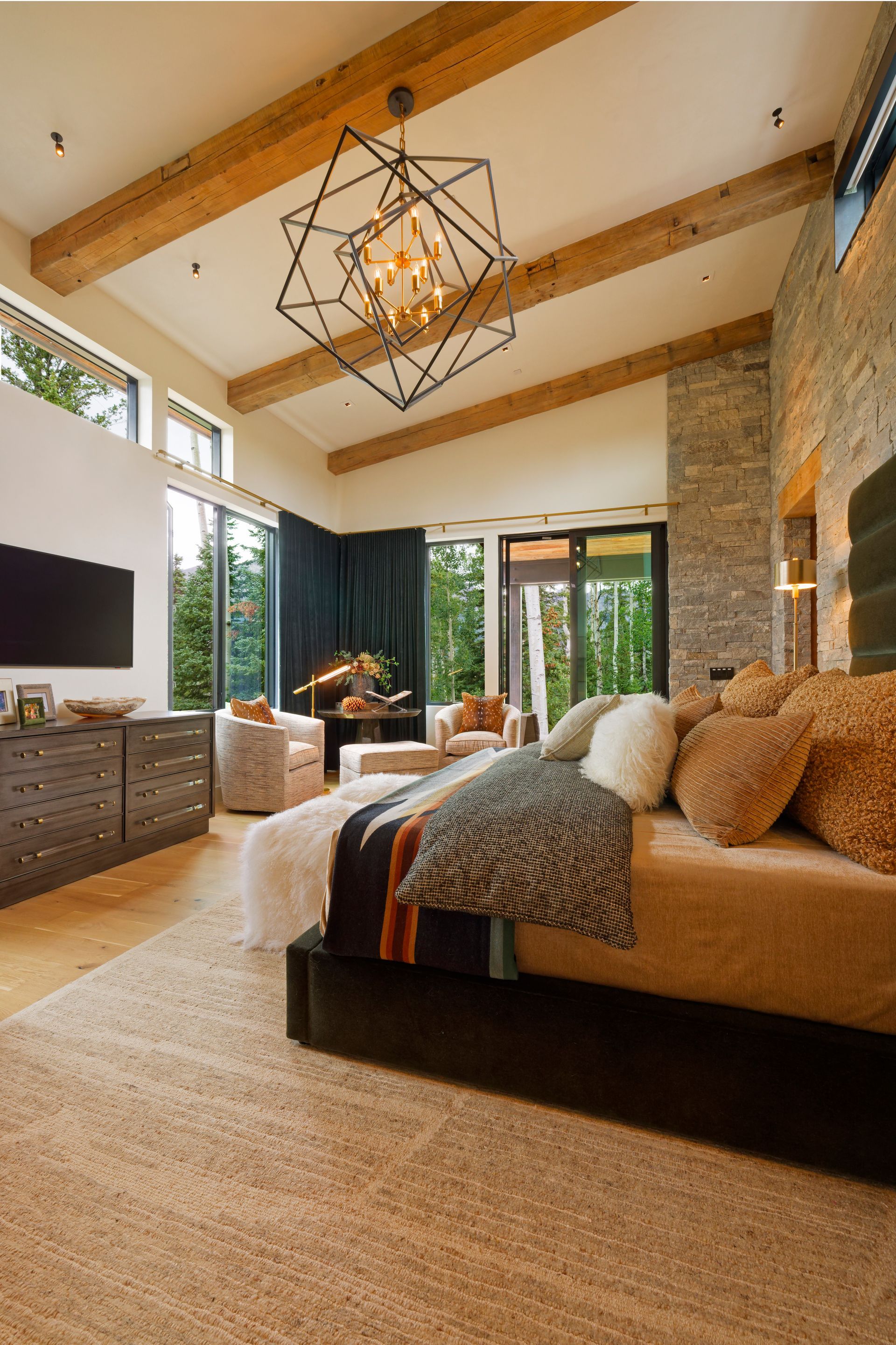 Bedroom with light wood floors, a bed, seating area, and windows with shutters.
