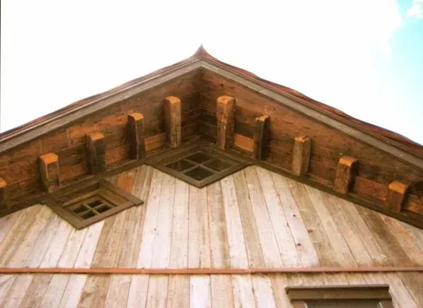 Wooden gable with decorative dark brown beams and small diamond-shaped windows, against a light sky.