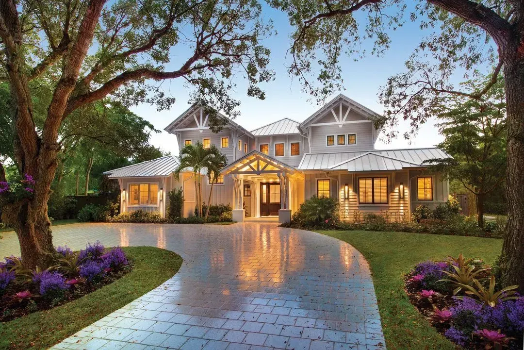 White two-story house with a brick walkway and green lawn. Balcony with hanging lights.