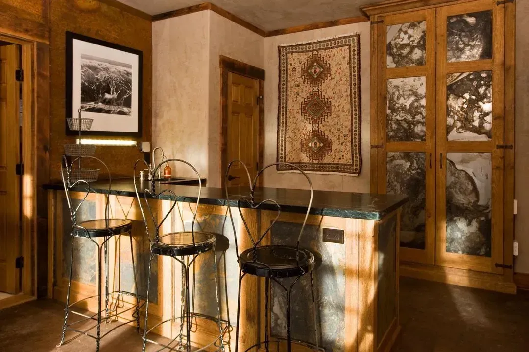 Bar area with granite counter, chrome stools, wood cabinets, and artwork.