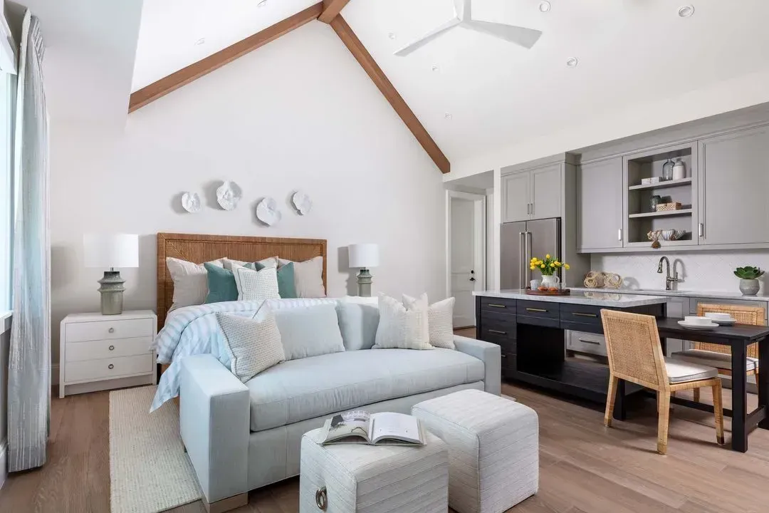 Bright studio apartment with bed, kitchen, and dining area. Light blue and white color scheme, vaulted ceiling.