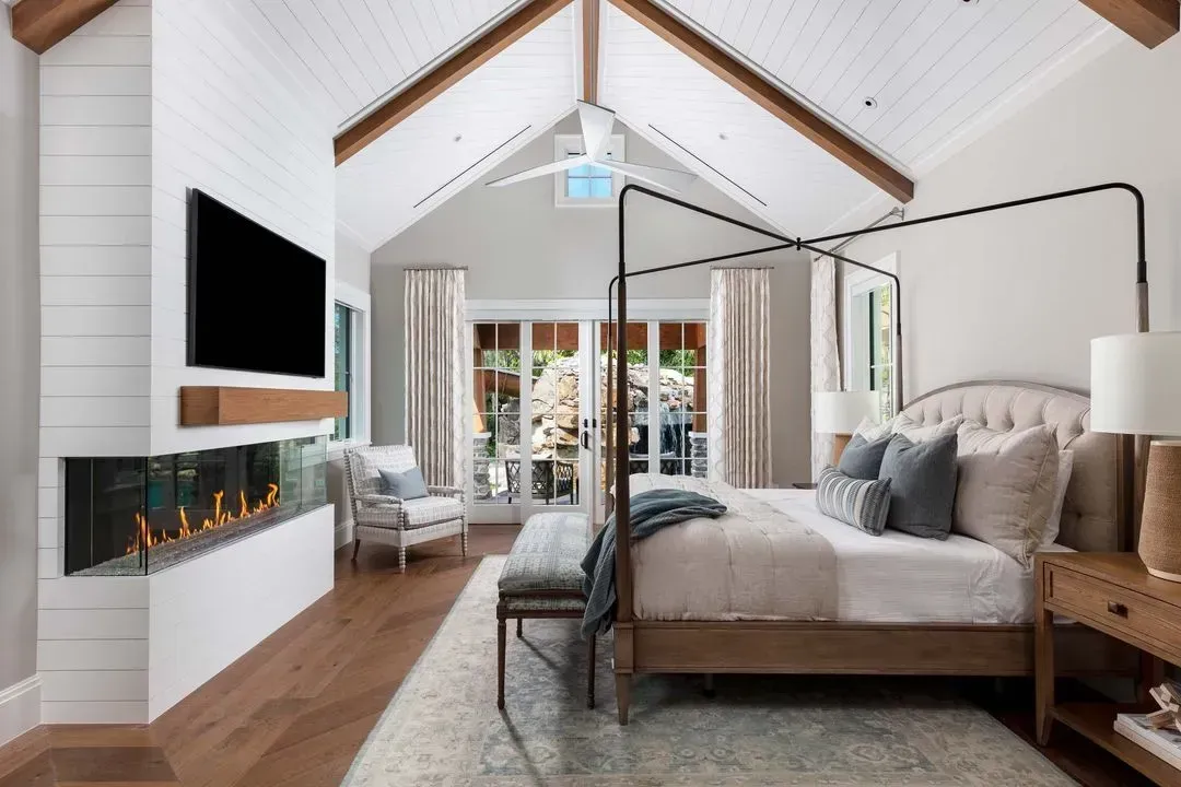 Master bedroom with a fireplace and vaulted ceiling, bed with a canopy, light and airy.