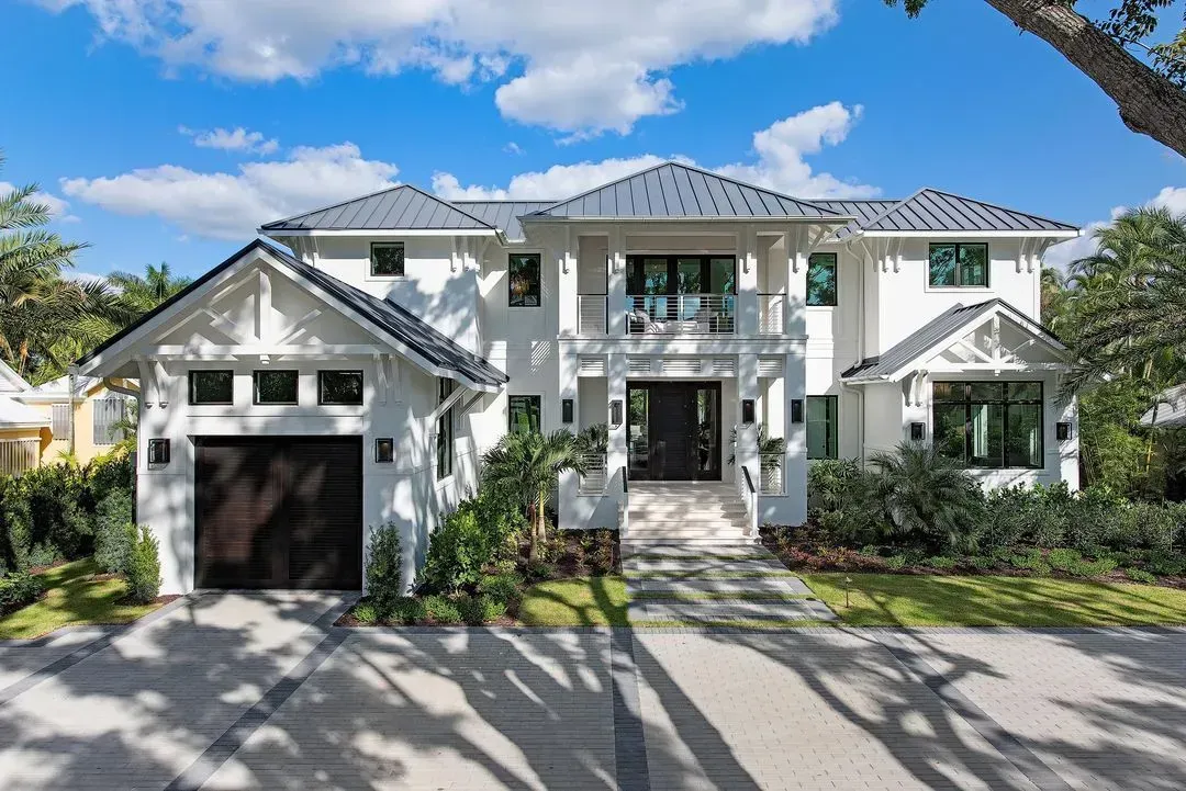 White two-story house with gray roof, garage, and walkway; blue sky with clouds.