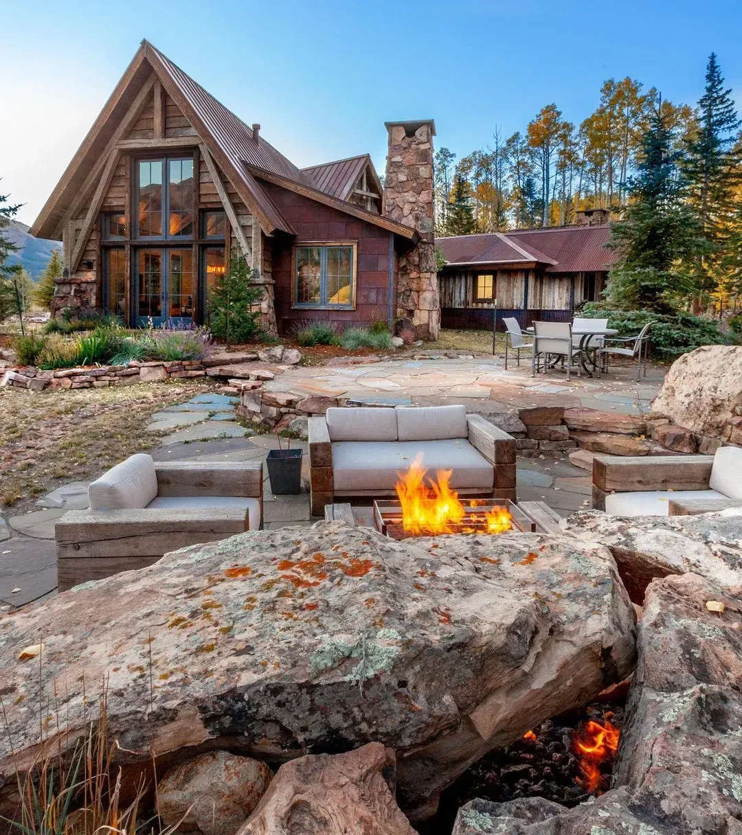Rustic cabin with outdoor seating area, fire pit, and autumn trees.