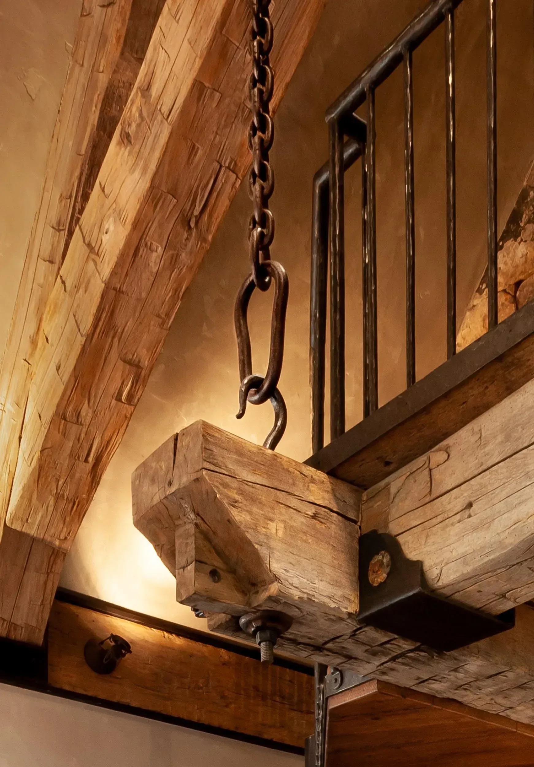 Wooden beam with a chain hanging from it. Wrought iron railing in background.