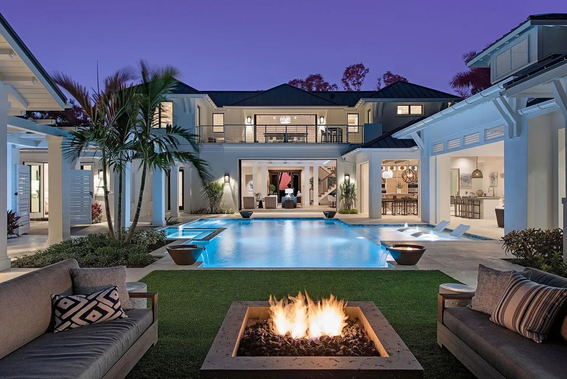 Luxury home exterior with pool and fire pit at dusk.