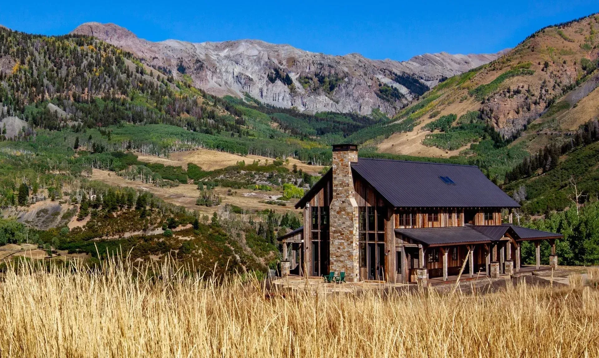 Stone cabin nestled in a valley with mountains in the background and tall grass in the foreground.