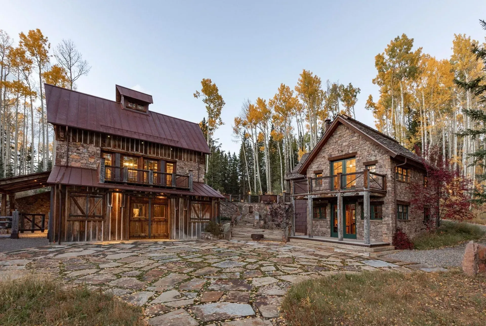 Rustic stone and wood buildings in a forest setting with a stone courtyard. Autumn trees.