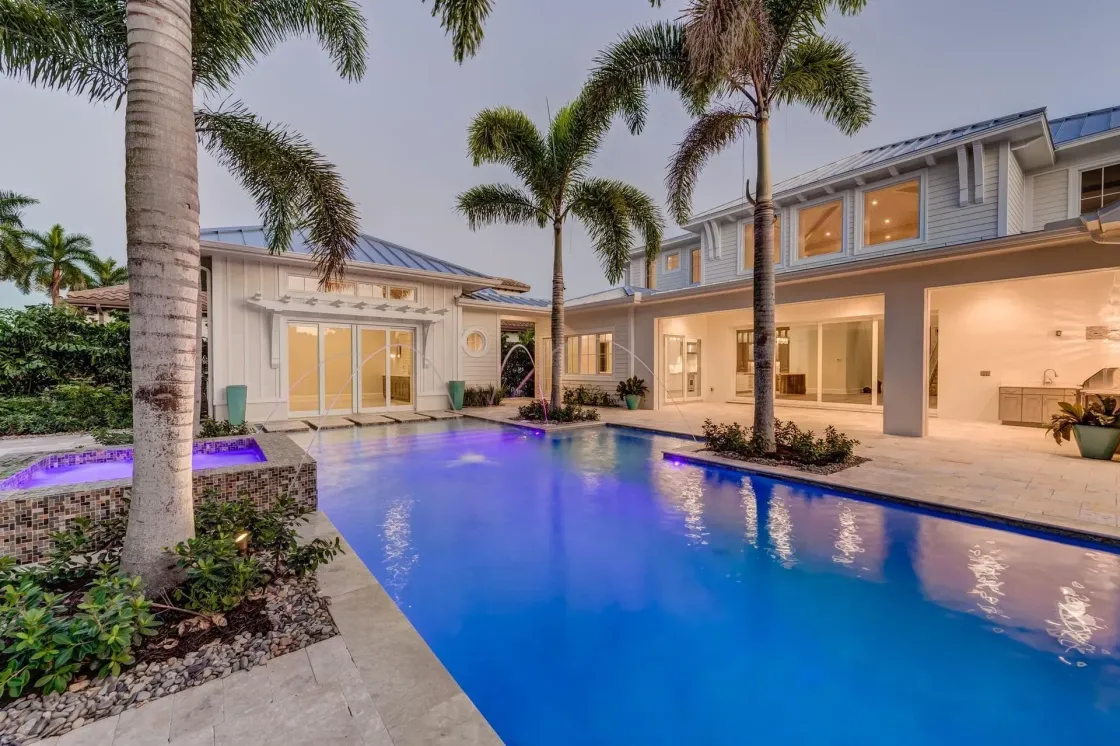 Luxurious home with pool, palm trees, and nighttime lighting; white walls, blue water.