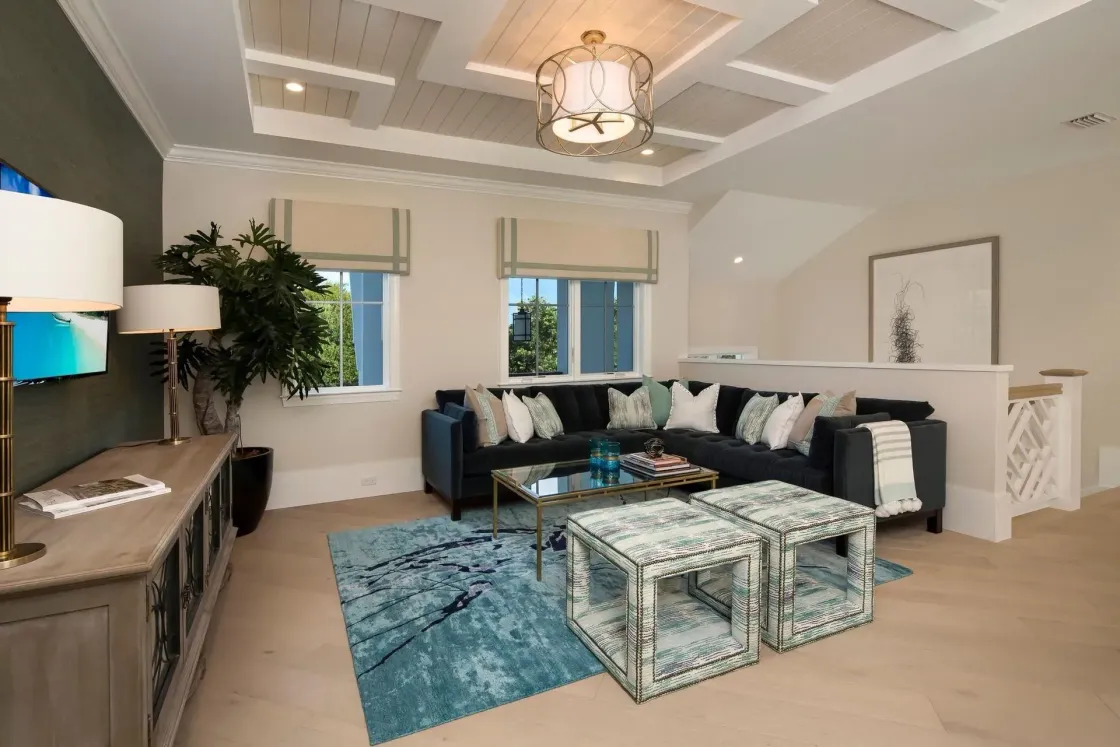 Living room with blue sectional, teal rug, and ottomans, neutral walls, and a coffered ceiling.