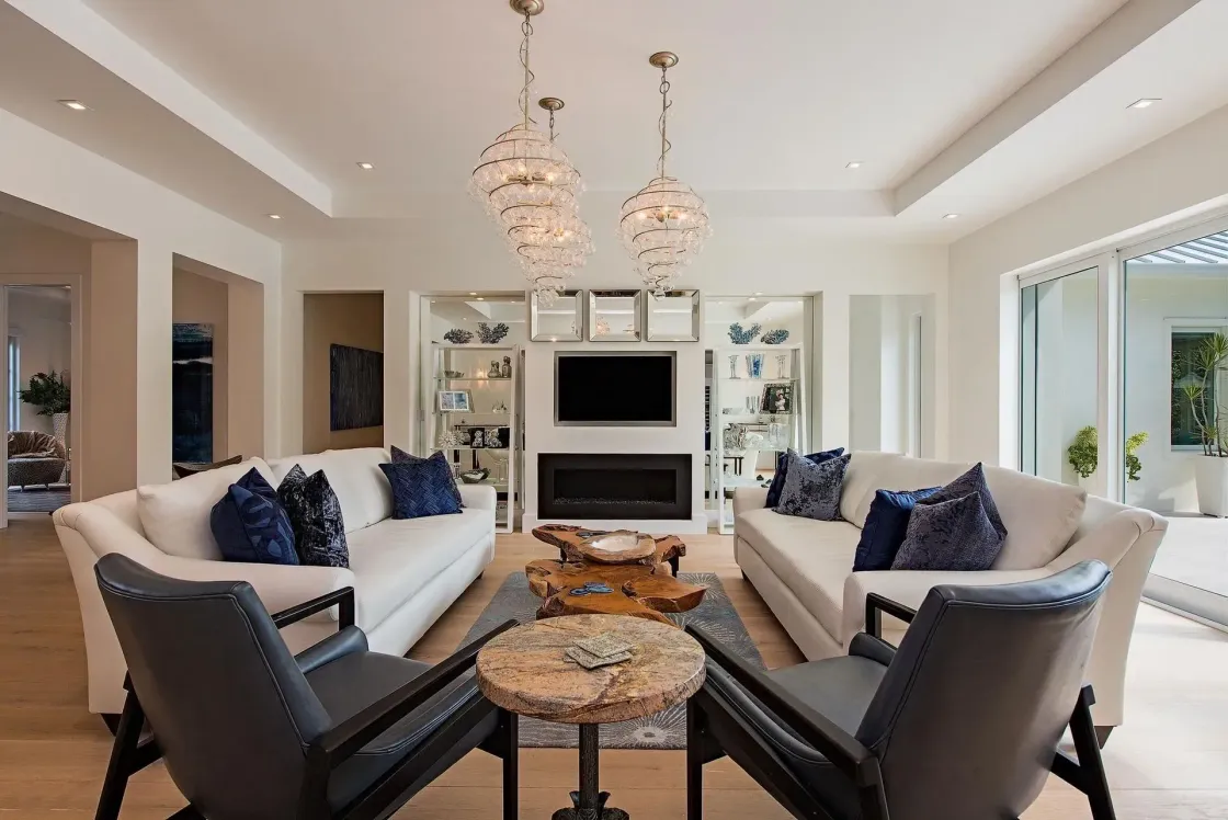 Bright living room with two white sofas, black chairs, fireplace, and chandeliers.