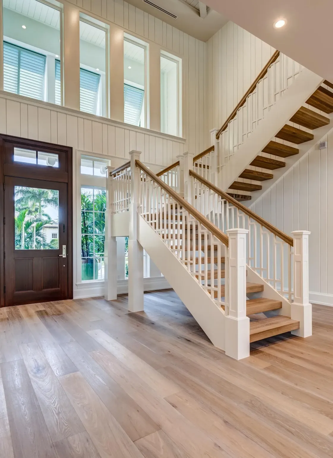 Interior with staircase, wooden floors, white walls, and a dark brown front door.