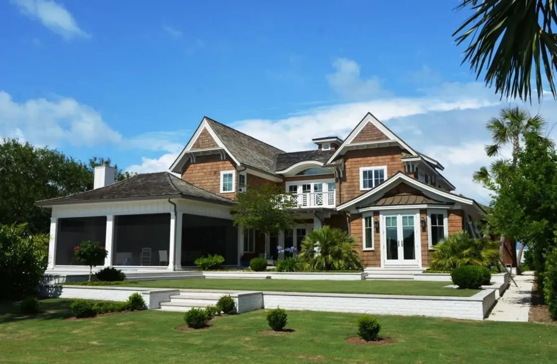 Brown and white two-story house with green lawn, blue sky, and palm trees.