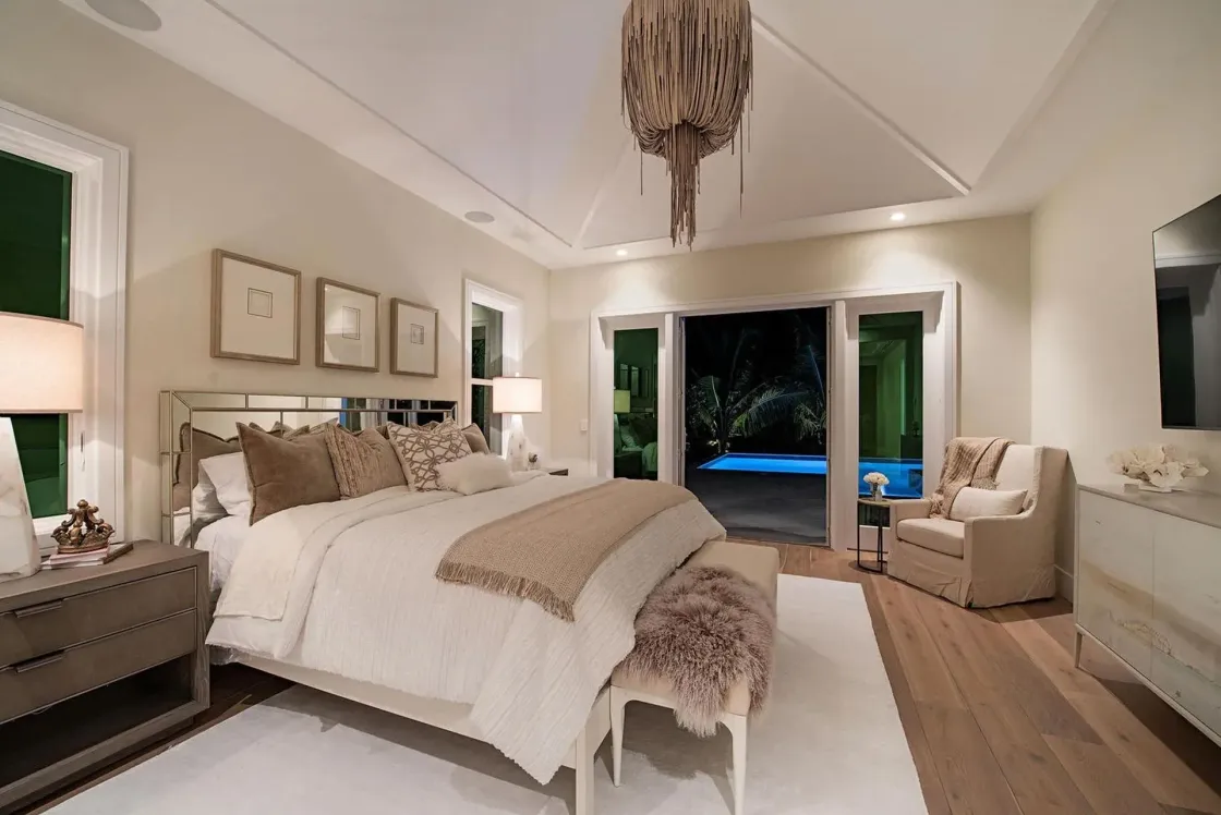 Bedroom with a bed, bench, and armchair. French doors lead to a pool.
