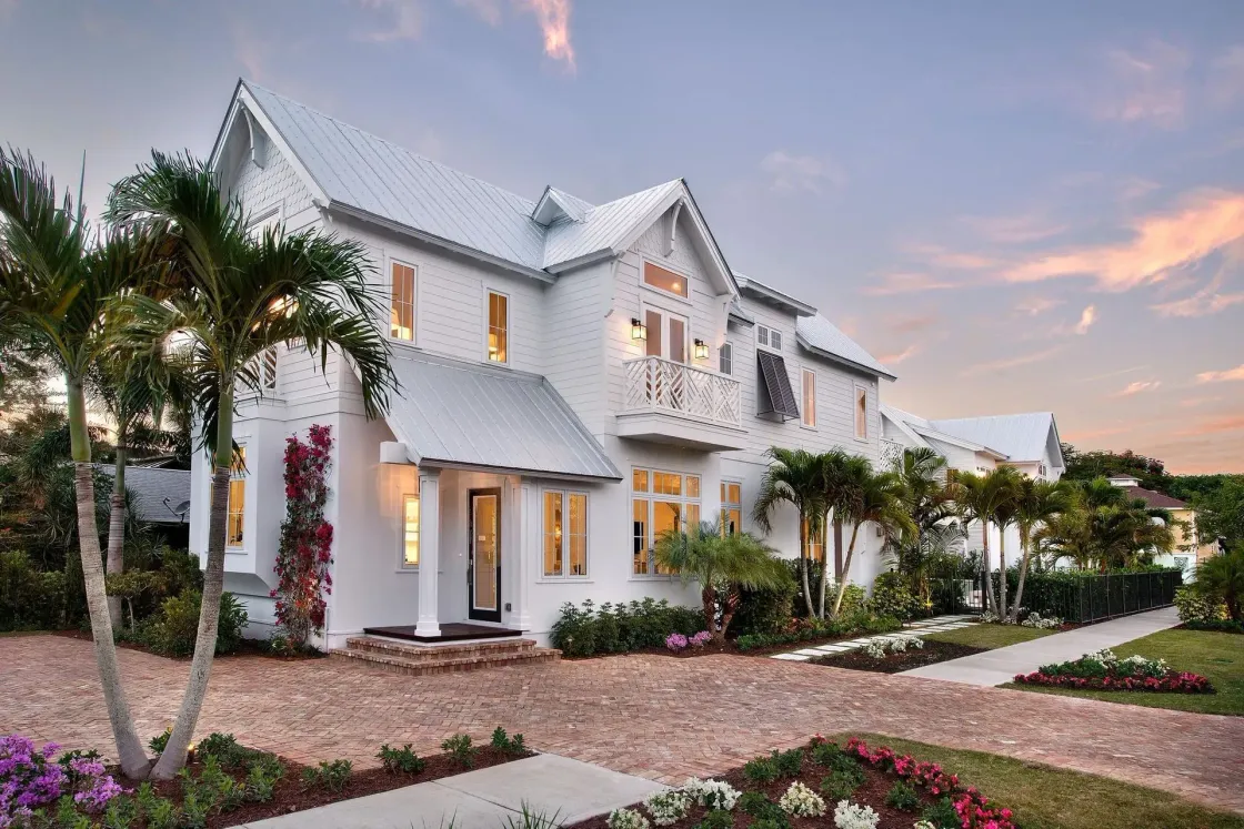 White multi-story house with palm trees, gravel driveway, and a sunset sky.