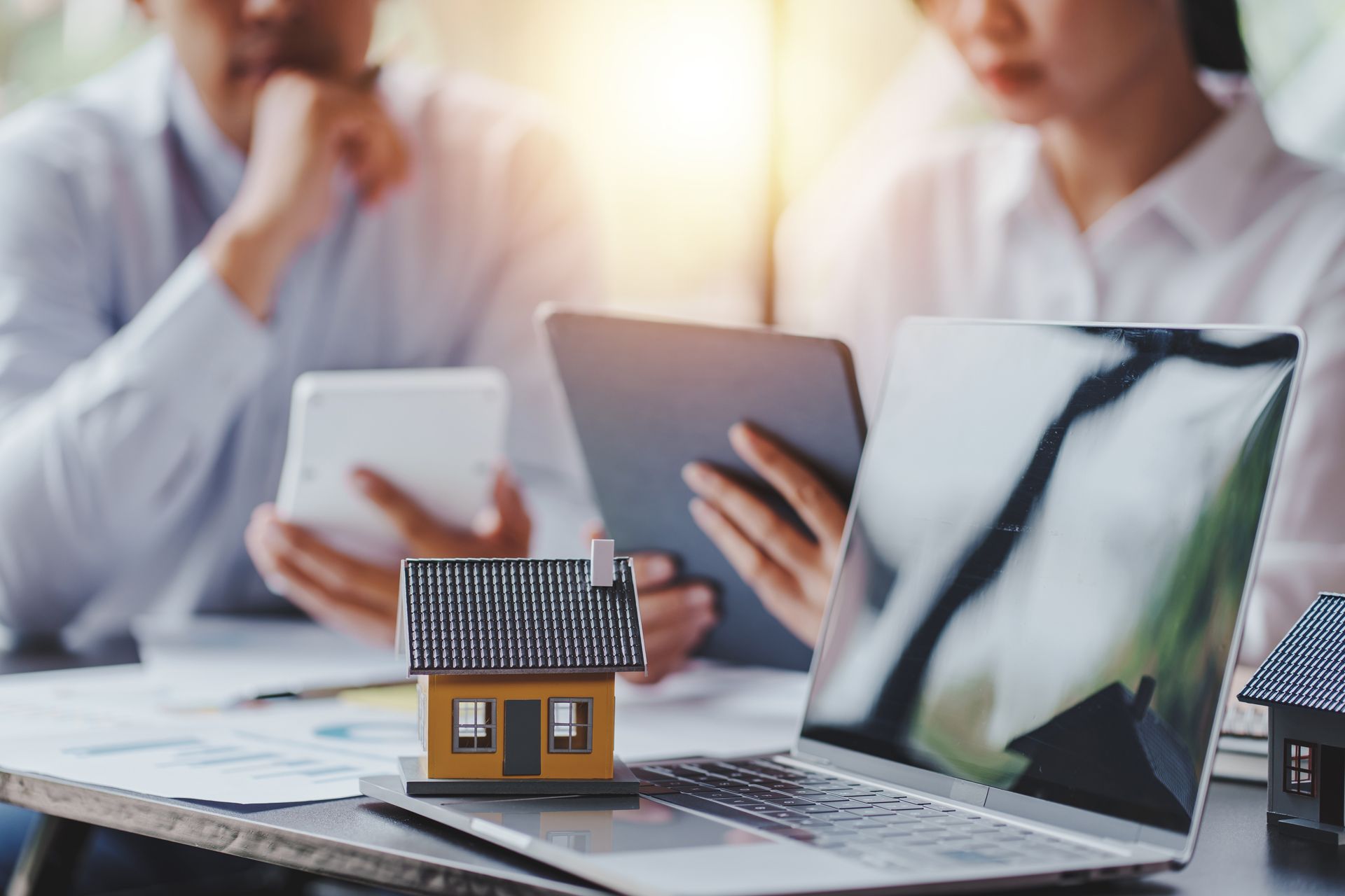 Two people reviewing documents and a laptop with a small model house on the keyboard