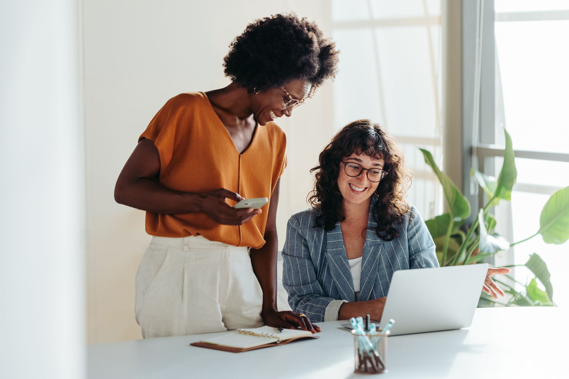 Two people collaborating at a desk with a laptop in a bright office