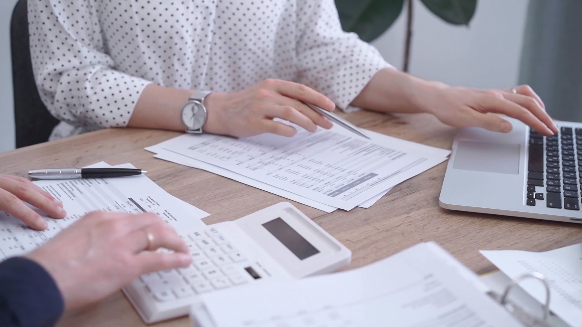 Hands reviewing paperwork beside a laptop on a desk