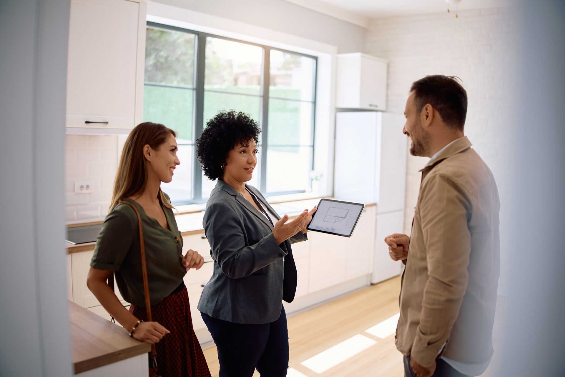 Three people discussing a tablet in a bright, modern kitchen-living space