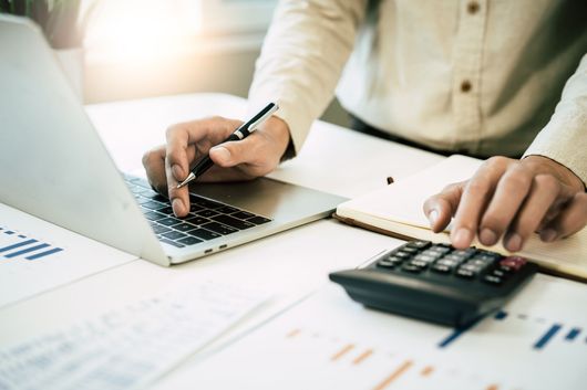 Hands using laptop, calculator, and pen over financial documents on a desk
