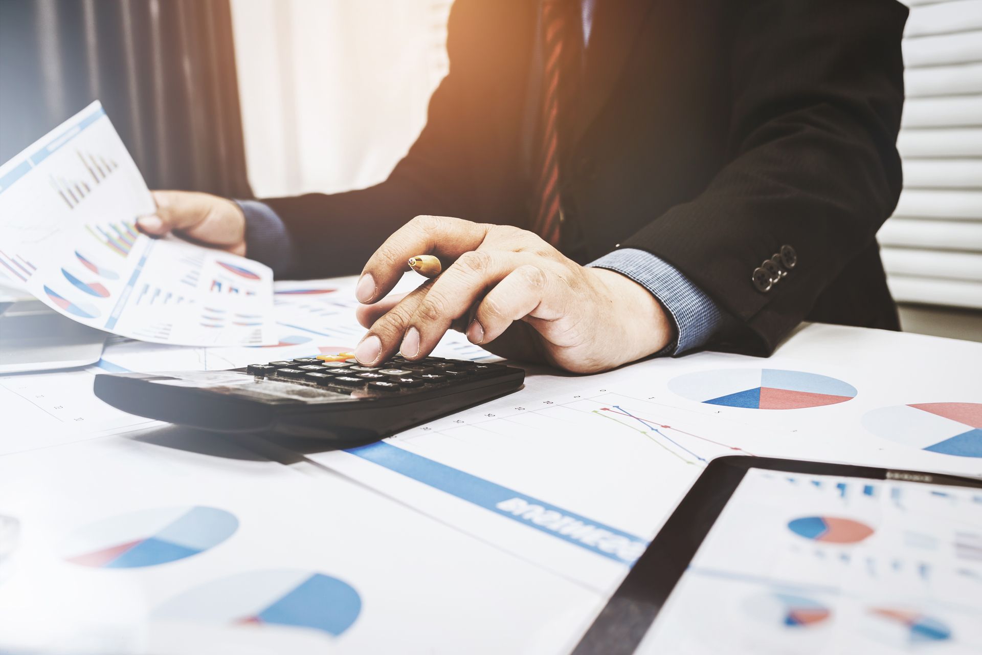 Hands using a calculator over financial charts and documents on a desk