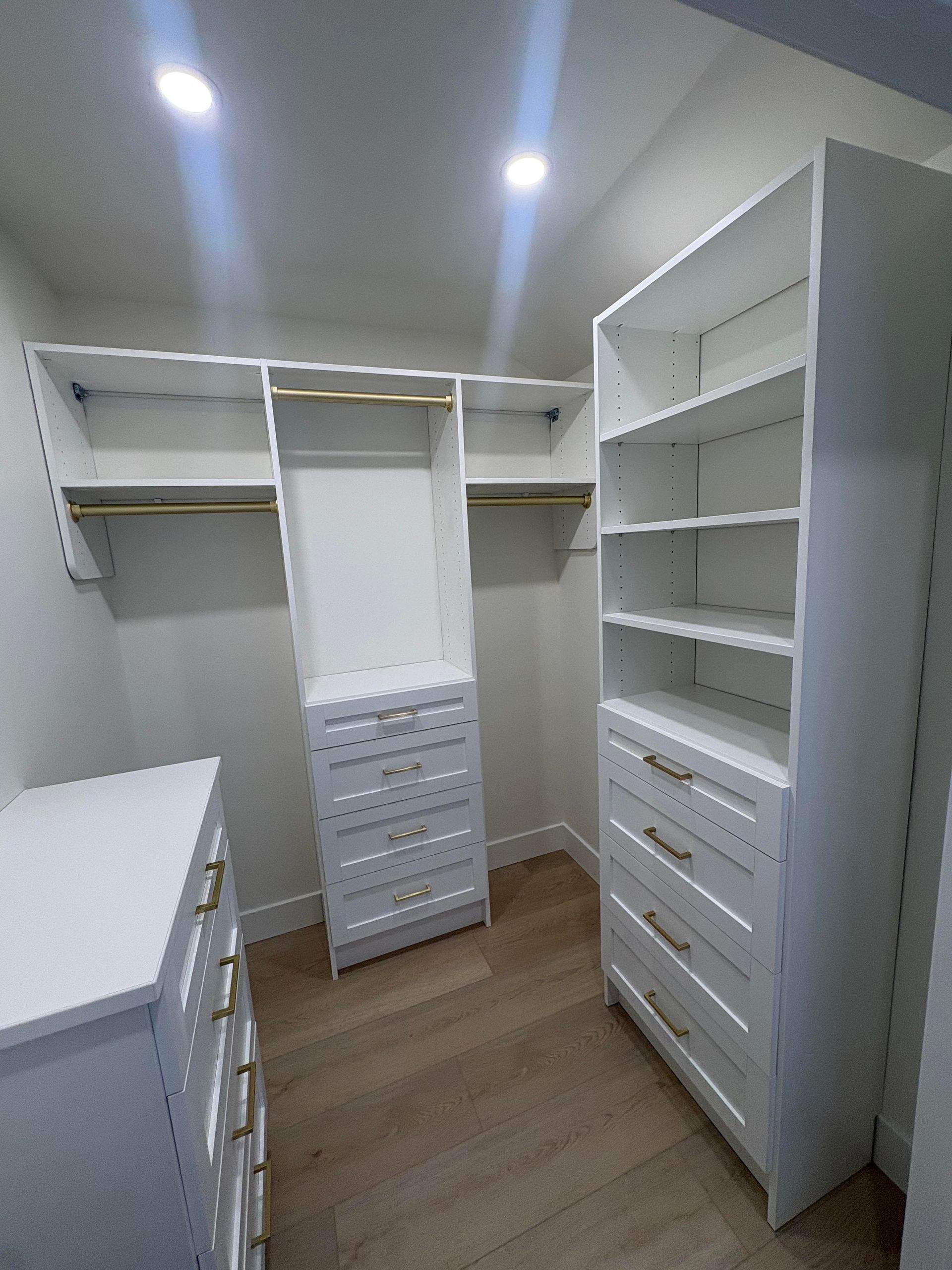 Walk-in closet with white built-in shelves, drawers, and hanging rods under ceiling lights