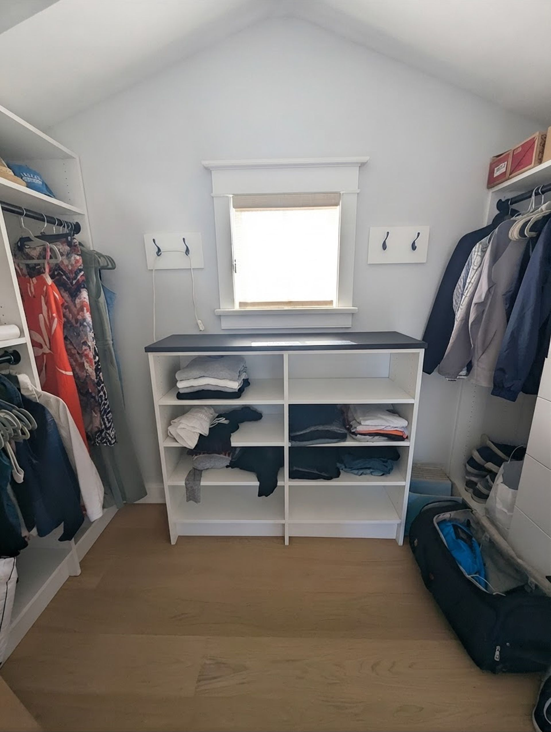 Walk-in closet with shelves, hanging clothes, folded items, and a small window.