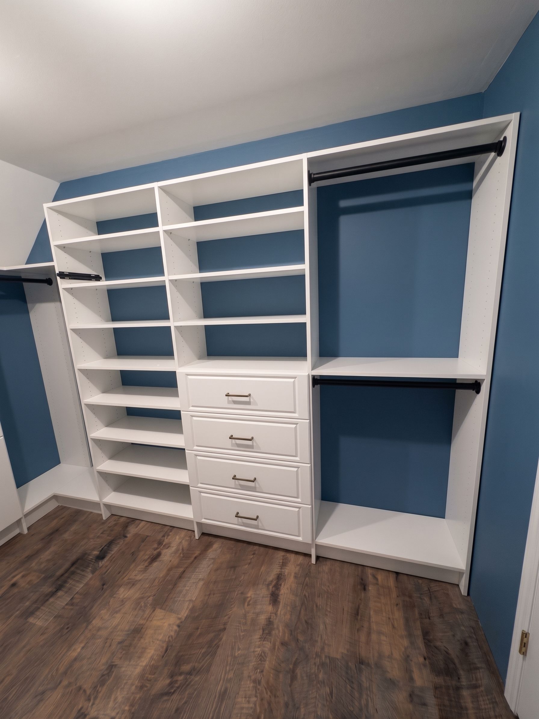 White built-in closet shelving with drawers and blue wall accents in a room with wood flooring
