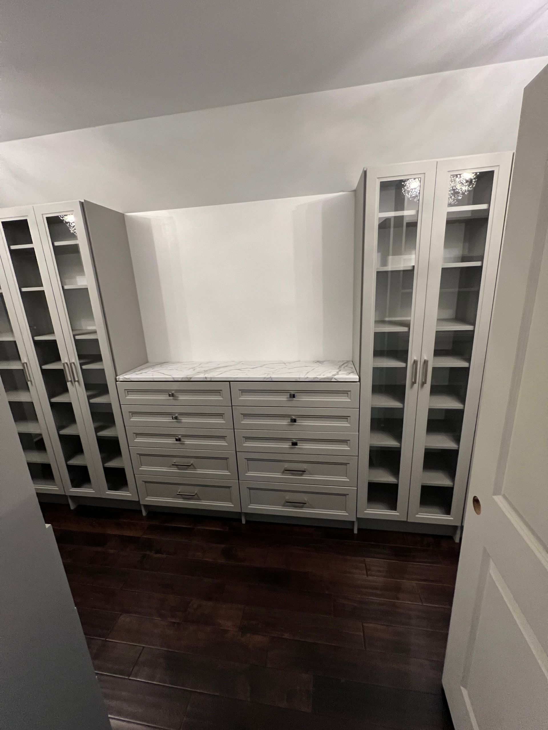 A room featuring light gray cabinetry, including two tall glass-door units flanking a central console with ten drawers.