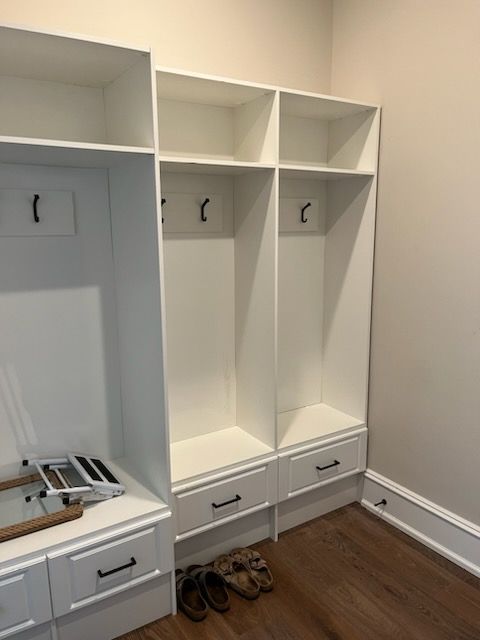 A white built-in mudroom locker system with open cubbies, coat hooks, and drawers above wood flooring.