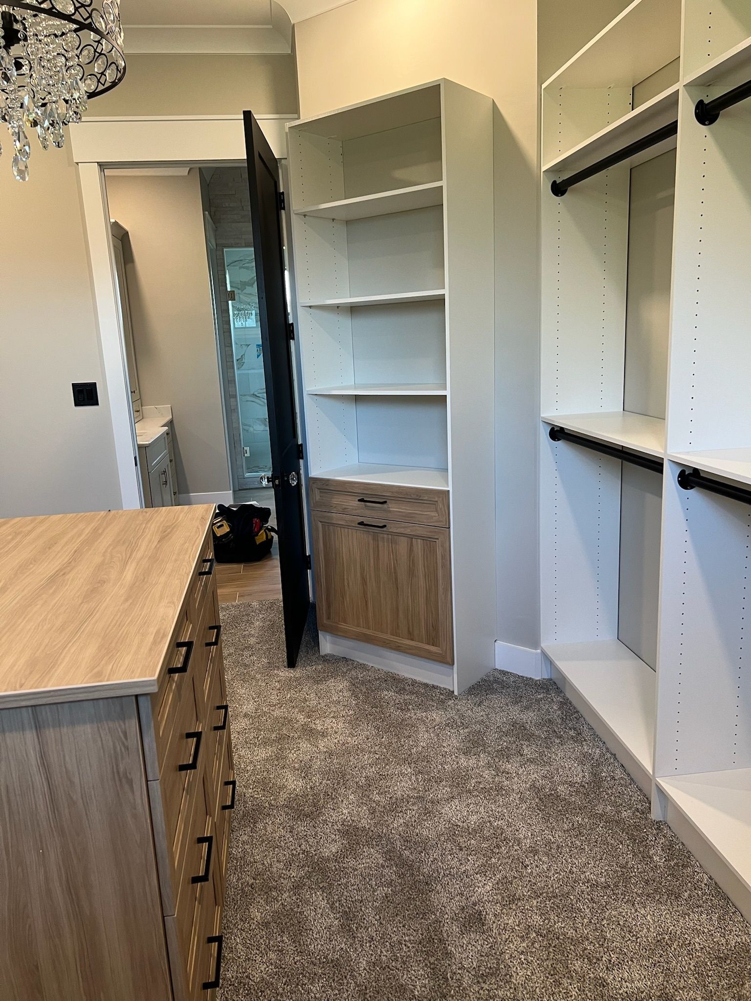 A walk-in closet featuring white open shelving, a wooden dresser, and a wooden cabinet with drawers on a carpeted floor.
