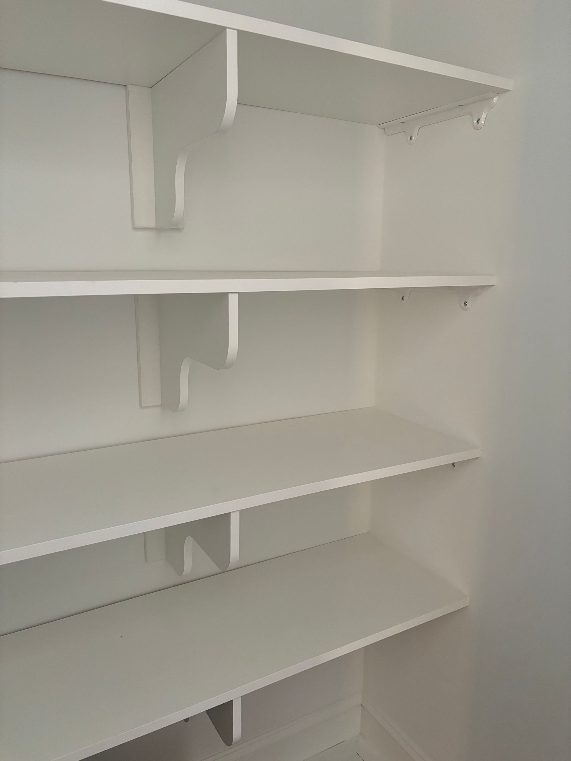 Four white, empty wooden shelves mounted on a white wall in a corner.