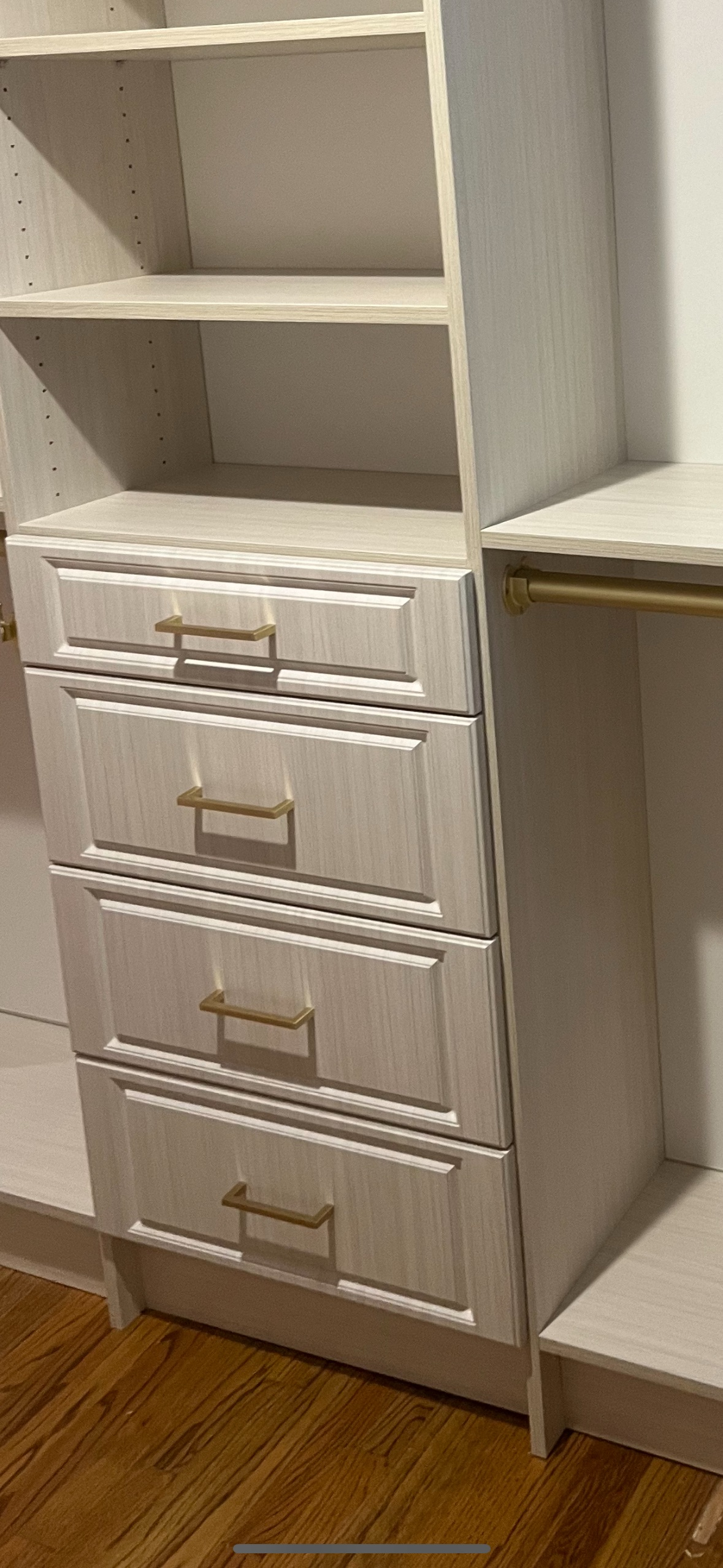 A white wooden closet organizer featuring four stacked drawers with gold handles and upper open shelving.
