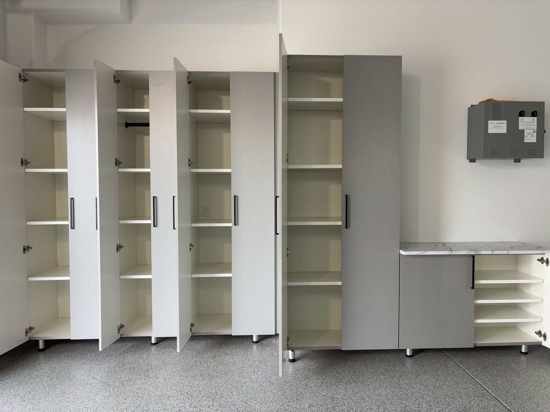 A row of tall white and grey storage cabinets against a white wall, with a small matching counter and shoe rack on the right.