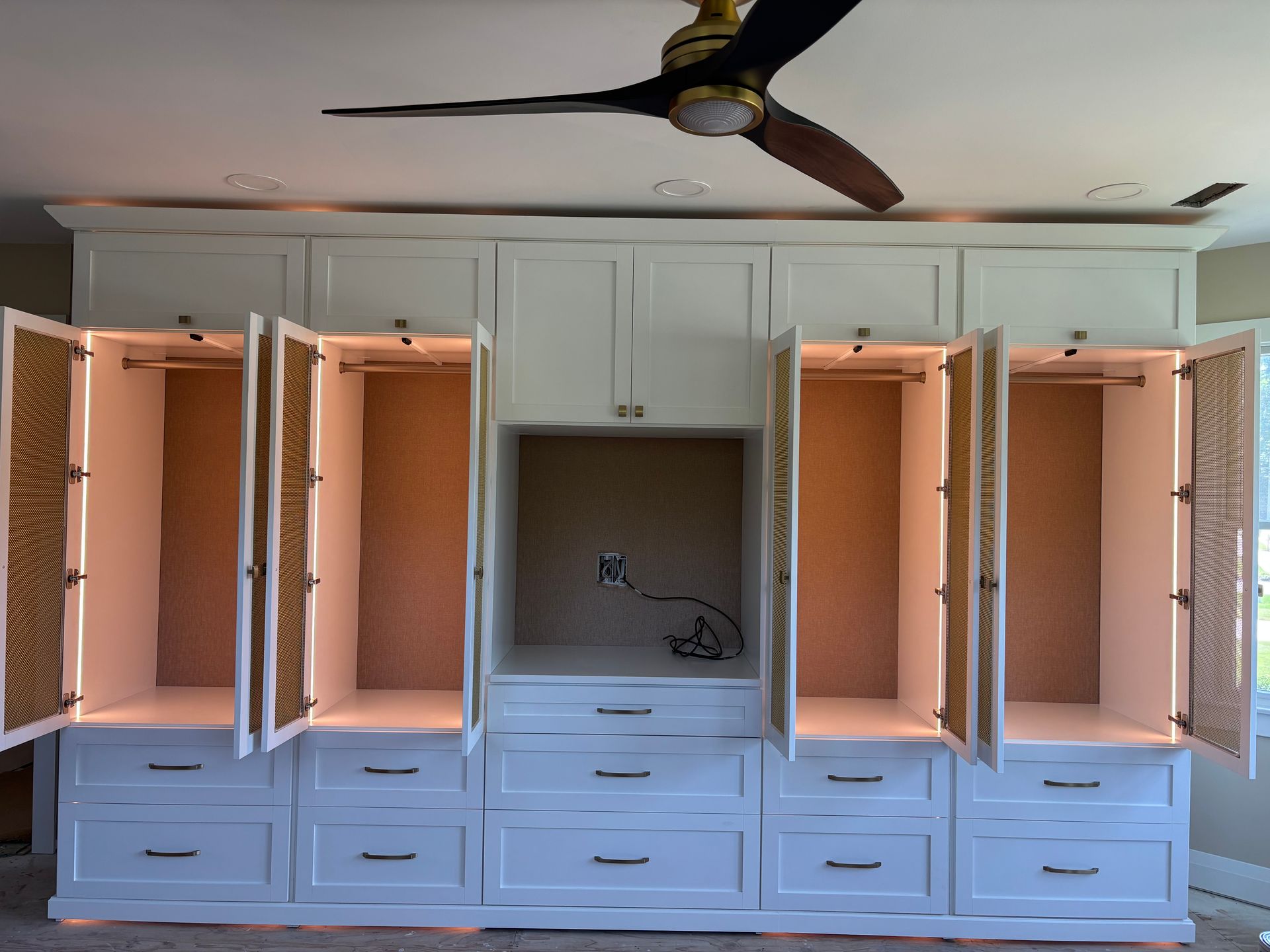 Open white built-in closet with drawers, shelves, and double doors in a bedroom, ceiling fan above.